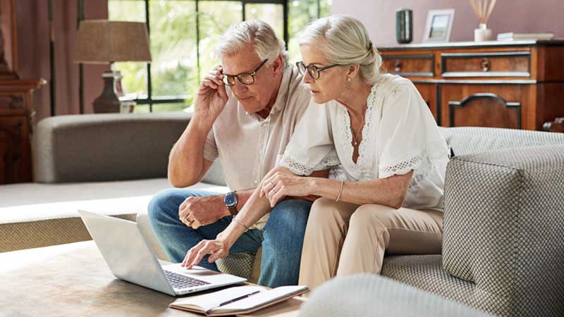um casal de reformados sentado no sofá com um computador em frente